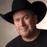 an up close photo of rodney carrington. he is wearing a black tshirt and black cowboy hat