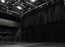A large black curtain hangs from the ceiling in front of a blank stage in the black box Kennedy Theatre