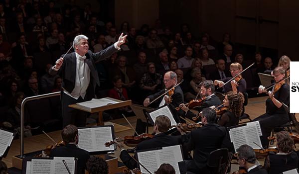 Conductor Grant Llewellyn stands in front of the Symphony holding a conductor's wand. The North Caorlina Symphony logo is placed in the lower right hand corner.